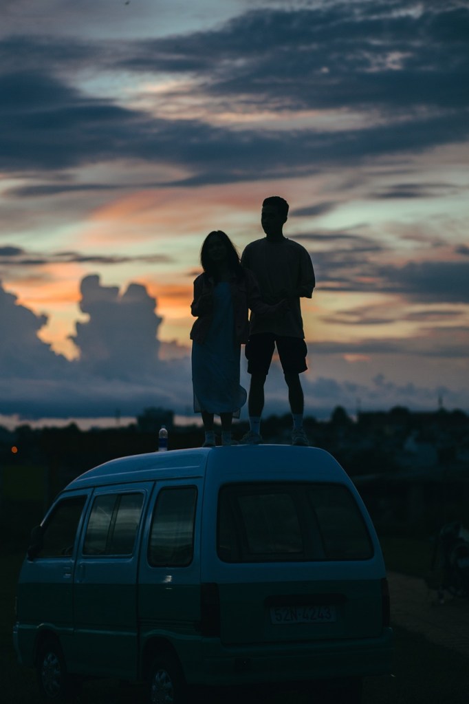 A couple standing on a car at sundown looking at the clouds