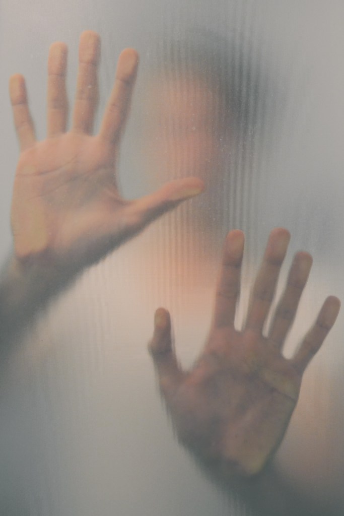 Person helpless, hands trying to escape through glass pane